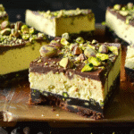 Close-up of a chocolate pistachio cheesecake bar topped with whole and chopped pistachios
