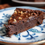 Slice of rich flourless chocolate cake topped with chopped hazelnuts